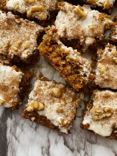 several pieces of cake sitting on top of a marble counter with white frosting and walnuts