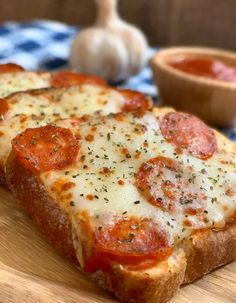 two slices of pizza sitting on top of a wooden cutting board next to a bowl of sauce