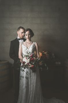 a bride and groom standing next to each other in front of a wine cask