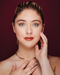 a woman with blue eyes wearing a gold choker and holding her hand near her face