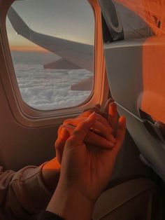 a person holding their hand up to the window of an airplane as it flies above the clouds