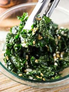 a glass bowl filled with spinach and other food on top of a wooden table