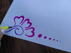 a person is drawing on a piece of white paper with purple ink and a yellow marker