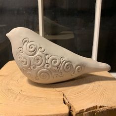 a ceramic bird sitting on top of a piece of wood