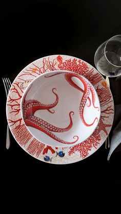 a plate with an octopus painted on it next to a wine glass and silverware