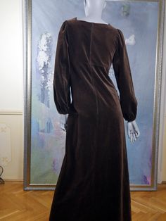 This stunning 70s brown velvet maxi dress has a square neckline and puffed long sleeves with elasticated cuffs, which you can also push up for a fuller look (see pictures). The Elizabethan-style long dress has an empire waistline and an A-line maxi skirt with an elegant fall. The dress features a padded front bodice with a diamond stitched pattern and velvet and ribbon wide braiding in pale pink, green, and gold that edges the front neckline and continues with long flowing ribbons almost to the Fall Fitted Velvet Maxi Dress, Fitted Velvet Maxi Dress For Fall, Velvet Maxi Dress For Fall, Vintage Brown Maxi Dress For Fall, Fall Maxi Dress With Gathered Sleeves And Fitted Bodice, Fall Maxi Dress With Gathered Sleeves And Fitted Design, Fall Gathered Sleeves Fitted Maxi Dress, Fall Fitted Maxi Dress With Gathered Sleeves, Fall Maxi Dress With Gathered Sleeves