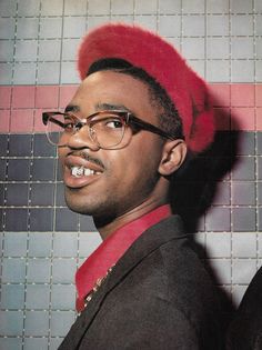 a man wearing glasses and a red hat in front of a tiled wall with pink tiles