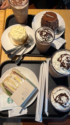 three desserts and drinks are on trays with forks, spoons and napkins