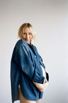 a pregnant woman posing for the camera with her shirt over her body and jeans jacket on