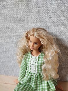 a doll with blonde hair wearing a green and white checkered dress sitting on a wooden table