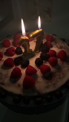 a cake with strawberries and raspberries on it, lit by two candles