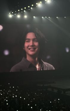 a man is smiling while standing in front of a large screen on the stage at a concert