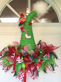 a green christmas tree wreath with red and green decorations on the top, hanging in front of a white door