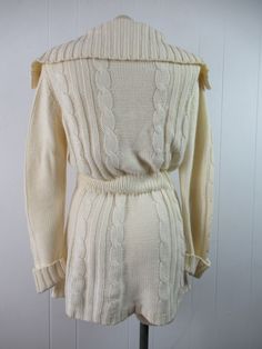 "Vintage 1970s sweater. Made of Acrylic knit. Color is cream white. Bohemian hippy style. Has a button down front, wooden buttons, large cowl style collar, internal cinches waist belt and two lower pockets. Made by F.O.B./ N.Y. About a size medium. Actual measurements are: 36\" at the bust 29\" at the waist 39\" at the hips 15.5\" shoulder seam to shoulder seam 28\" shoulder seam to cuff(with cuffs not rolled up) 33\" overall length In excellent condition." Vintage Cream Sweater For Fall, Fitted Vintage Sweater Coat With Long Sleeves, Long Fitted Cream Sweater, Fitted Long Sleeve Vintage Sweater Coat, Vintage Knit Sweater Coat With Long Sleeves, Vintage Knitted Sweater Coat With Long Sleeves, Vintage Long Sleeve Sweater With Buttons, Vintage Knit Sweater Coat, Vintage Knitted Long Sleeve Sweater Coat