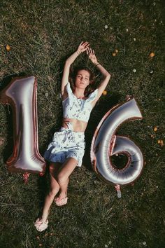 a woman laying in the grass with her hands behind her head and number six balloons