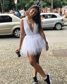 a woman in a white dress is walking down the street with a crown on her head