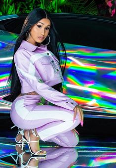 a woman sitting on the hood of a car in front of a holographic background