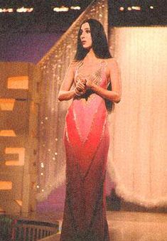 a woman in a red and pink dress standing on stage with her hands folded out