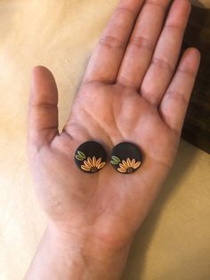 a person's hand holding two small black and yellow flower studs on them