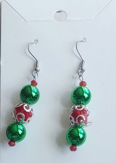 This pair of earrings is made with metallic green pearls and red rondelles. Silver-plated earring hooks and wire were used. Green Beaded Earrings For Christmas, Green Dangle Earrings For Holiday, Green Dangle Earrings For Holidays, Christmas Party Earrings With Round Beads, Christmas Party Round Beads Earrings, Christmas Party Round Bead Earrings, Green Beaded Earrings For Festive Occasions, Green Beaded Earrings For Holidays, Green Handmade Earrings For Holiday