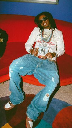 a woman sitting on top of a red couch wearing ripped jeans and white sneakers with her hands in her pockets