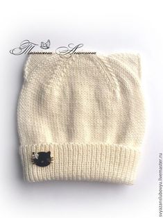 a white knit hat with a black cat on the front and back side, sitting on top of a white surface