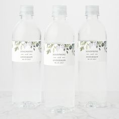 three water bottles with labels on them sitting on a marble countertop in front of a white wall