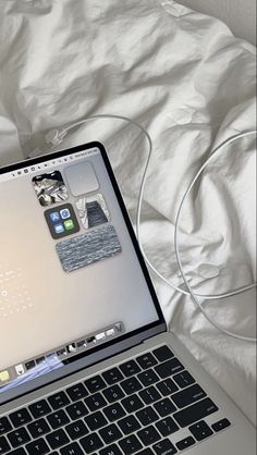 an open laptop computer sitting on top of a white bed next to a phone and headphones