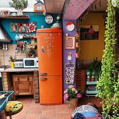 an orange refrigerator sitting in the middle of a kitchen next to a potted plant