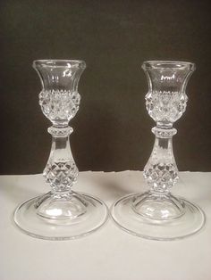 two clear glass candlesticks sitting on top of a white tableclothed surface