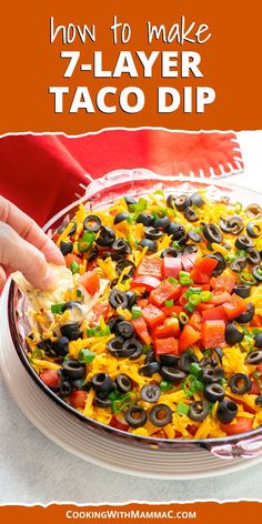 a person dipping tortilla into a bowl with black olives and peppers on top