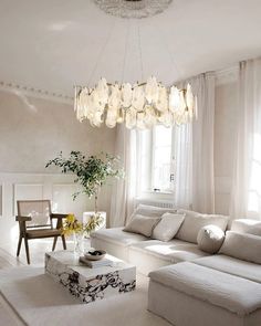 a living room filled with white furniture and a chandelier hanging from the ceiling