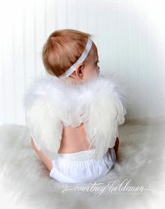 a baby with angel wings on her back is wearing a headband and white dress