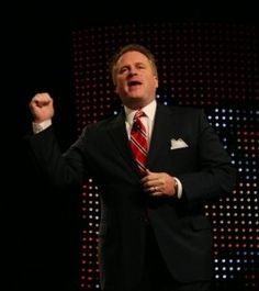 a man in a suit and tie standing on stage with his hands up to the side