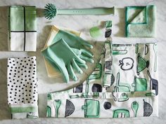 green and white kitchen accessories laid out on a marble counter top, including oven mitts, gloves, napkins, dish towel, and other items