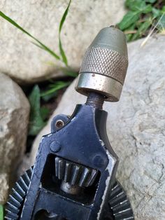 an old metal object sitting on top of a rock next to some grass and rocks