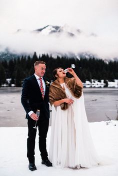 a bride and groom standing in the snow drinking water