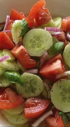 a white bowl filled with cucumber, tomatoes and onions on top of a table