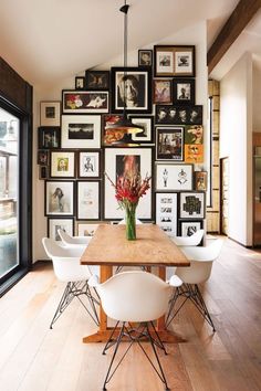 a dining room table with white chairs and framed pictures on the wall behind it in front of a large window