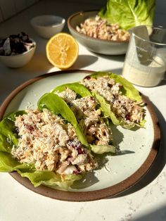 two lettuce wraps filled with tuna salad on top of a plate next to a bowl of fruit