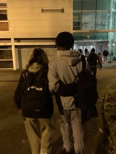 two people walking down the street at night with backpacks on their back and one person wearing a jacket