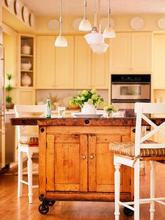 a kitchen island with two chairs and a table in the middle, surrounded by yellow cabinets