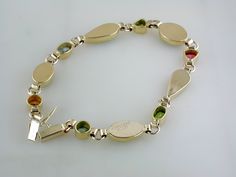 Ethiopian opals, topaz, tanzanite, citrine, peridot, tourmaline, green diopsite of various shapes and sizes are each delicately set in handmade bezels. This 14k yellow gold bracelet has been hand signed by the artist. 14K Yellow Gold & 22K Yellow Gold Ethiopian opals, topaz, tanzanite, citrine, peridot, tourmaline, green diopsite 7 1/4" long Plunger Clasp with figure 8 safety 9mm at widest point Weighs approximately 8.4 grams Hand Signed Available for Order. (Orders Placed today will ship in Bezel Set Diamond, Figure 8, Yellow Gold Bracelet, Ethiopian Opal, Bezel Setting, Citrine, Tourmaline, Topaz, Gold Bracelet