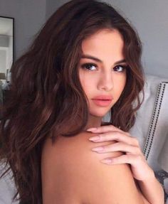 a woman with long brown hair is posing for the camera and has her hand on her chest