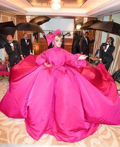 a woman in a pink dress and umbrellas on the floor with other people behind her