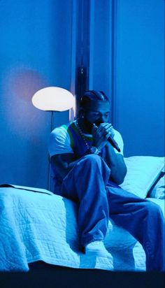 a man sitting on top of a bed talking on a cell phone in a blue room