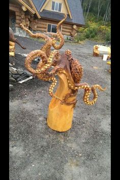 an octopus sculpture sitting on top of a wooden stump in front of a log cabin