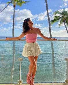 a woman standing on top of a balcony next to the ocean with palm trees in the background