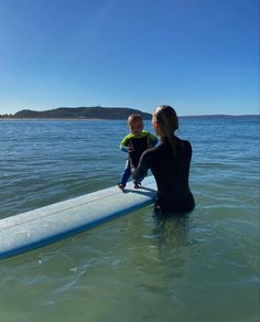 a woman and child sitting on a surfboard in the water