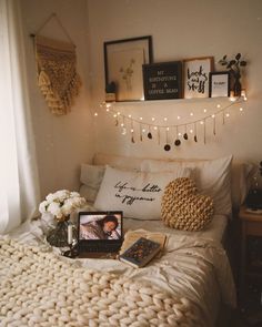 a white bed topped with pillows and blankets next to a window covered in string lights